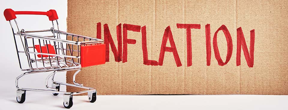 What causes inflation? Consumers inflation concept: a small model of a grocery shopping cart in front of a cardboard sign that has the word written "inflation" written across it in a red marker. It's the type of sign often associated with beggars on the street.